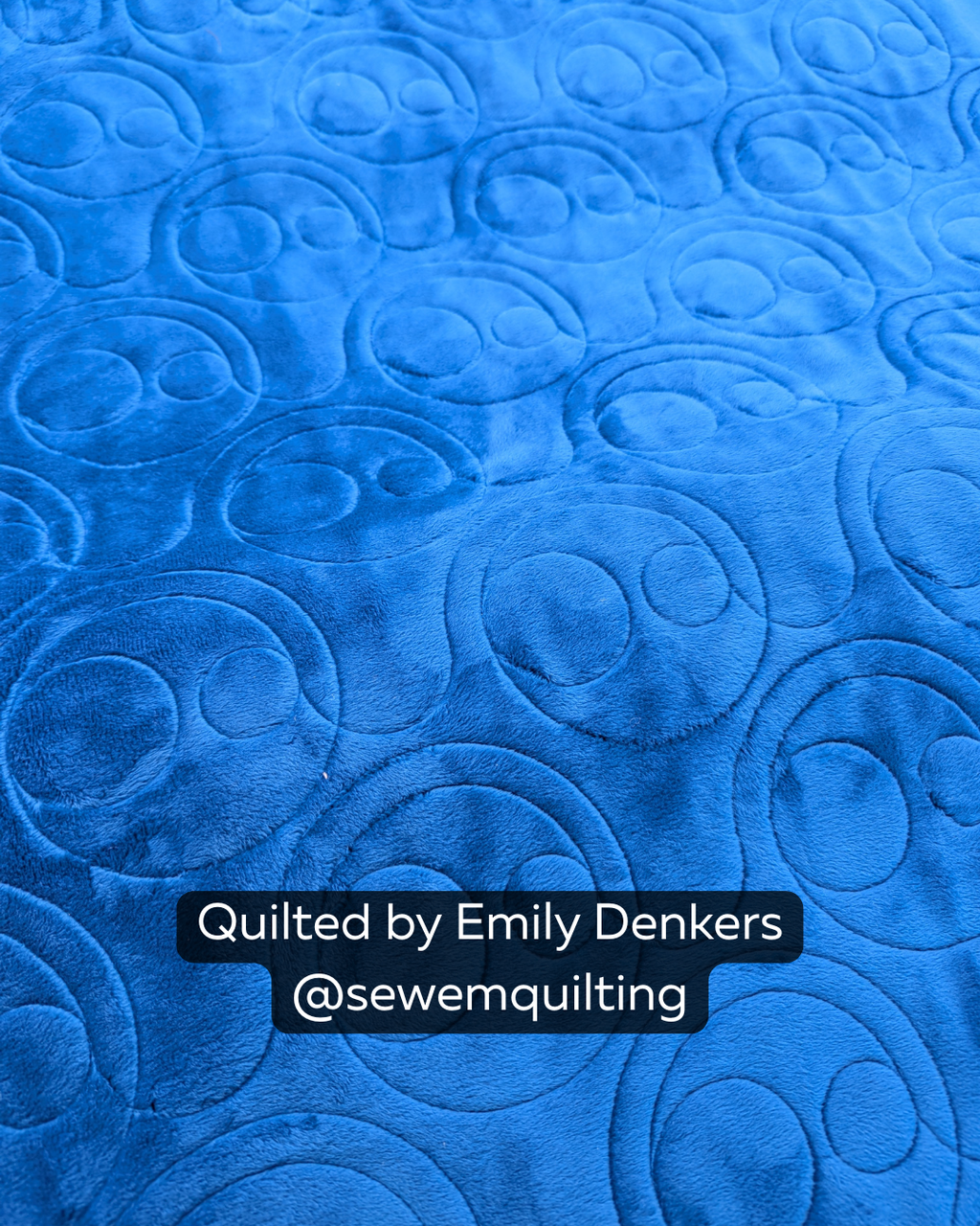 Close-up of a bright blue quilt featuring the Derpy Grin quilting pantograph, with playful smiley faces stitched in a continuous edge-to-edge design.