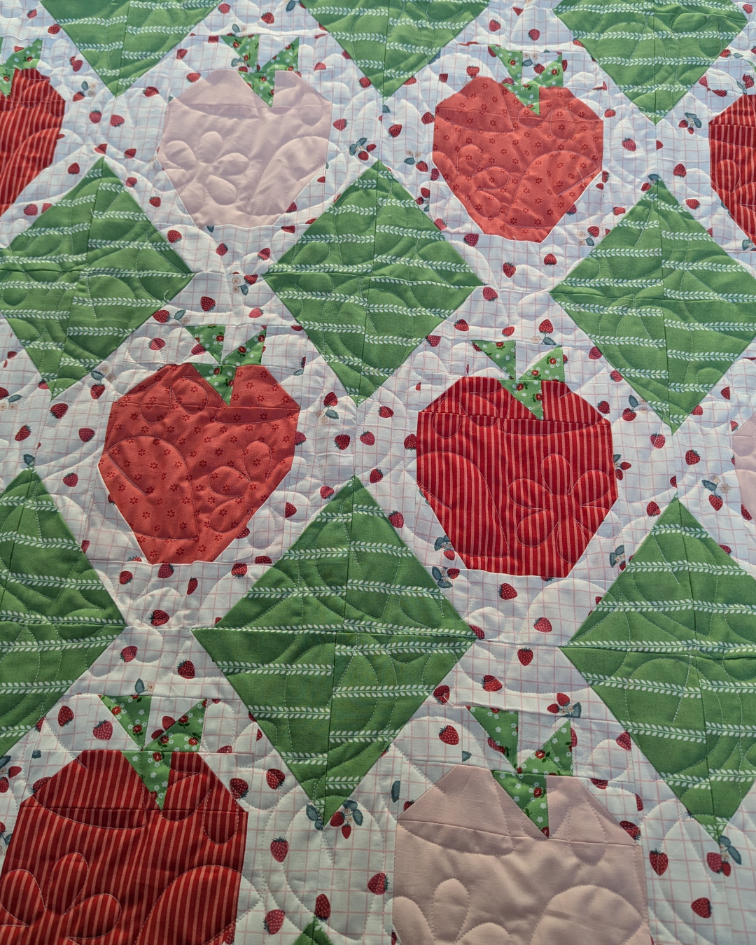 Finished strawberry patchwork quilt featuring the Trailing Vine quilting pantograph, with flowing leaves and flower motifs stitched edge to edge across red, pink, and green blocks.
